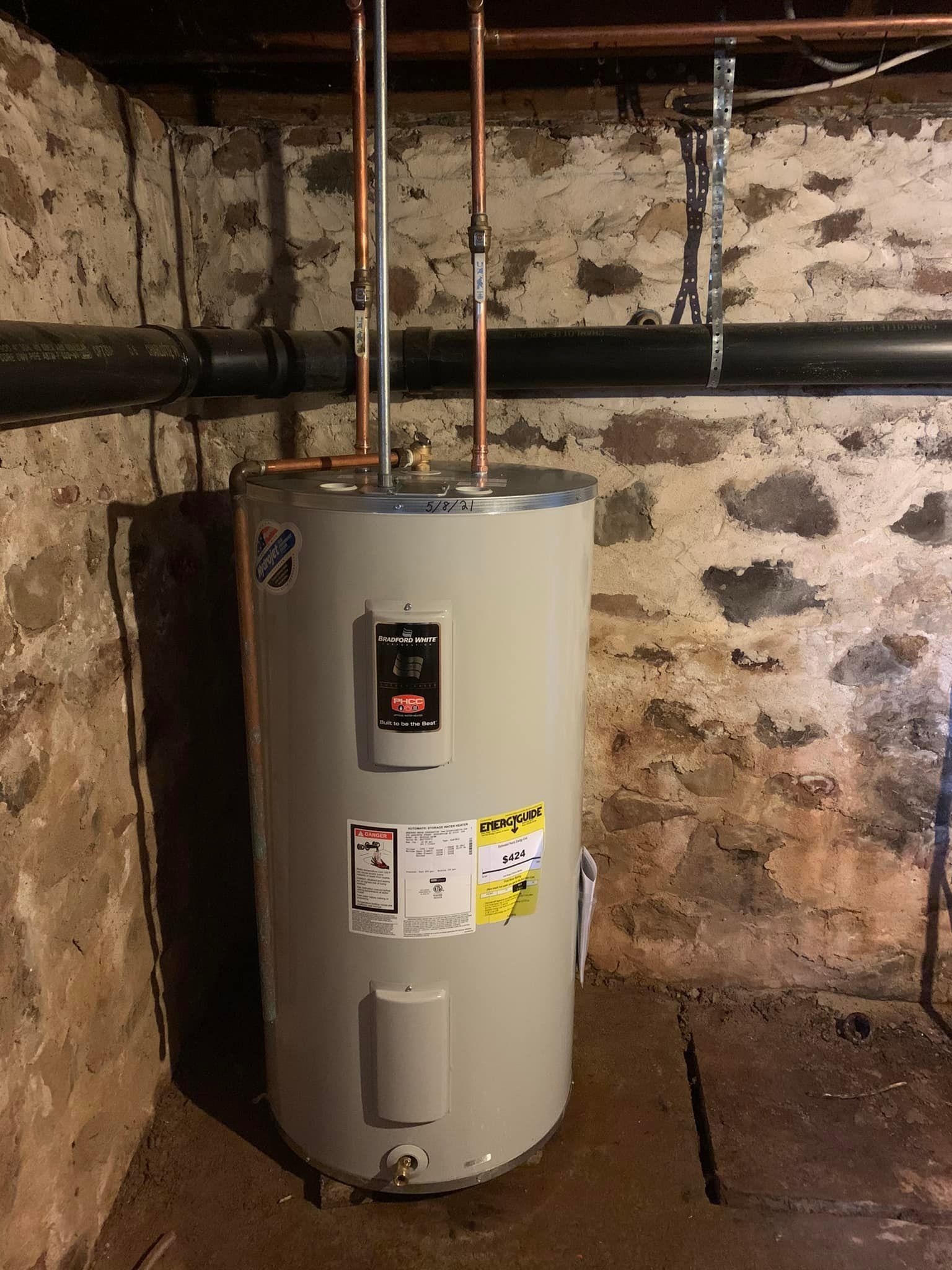 A water heater is sitting in a basement next to a stone wall.