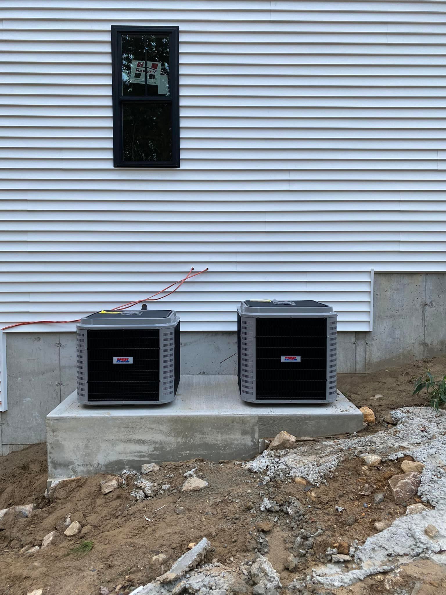 Two air conditioners are sitting on the side of a house.