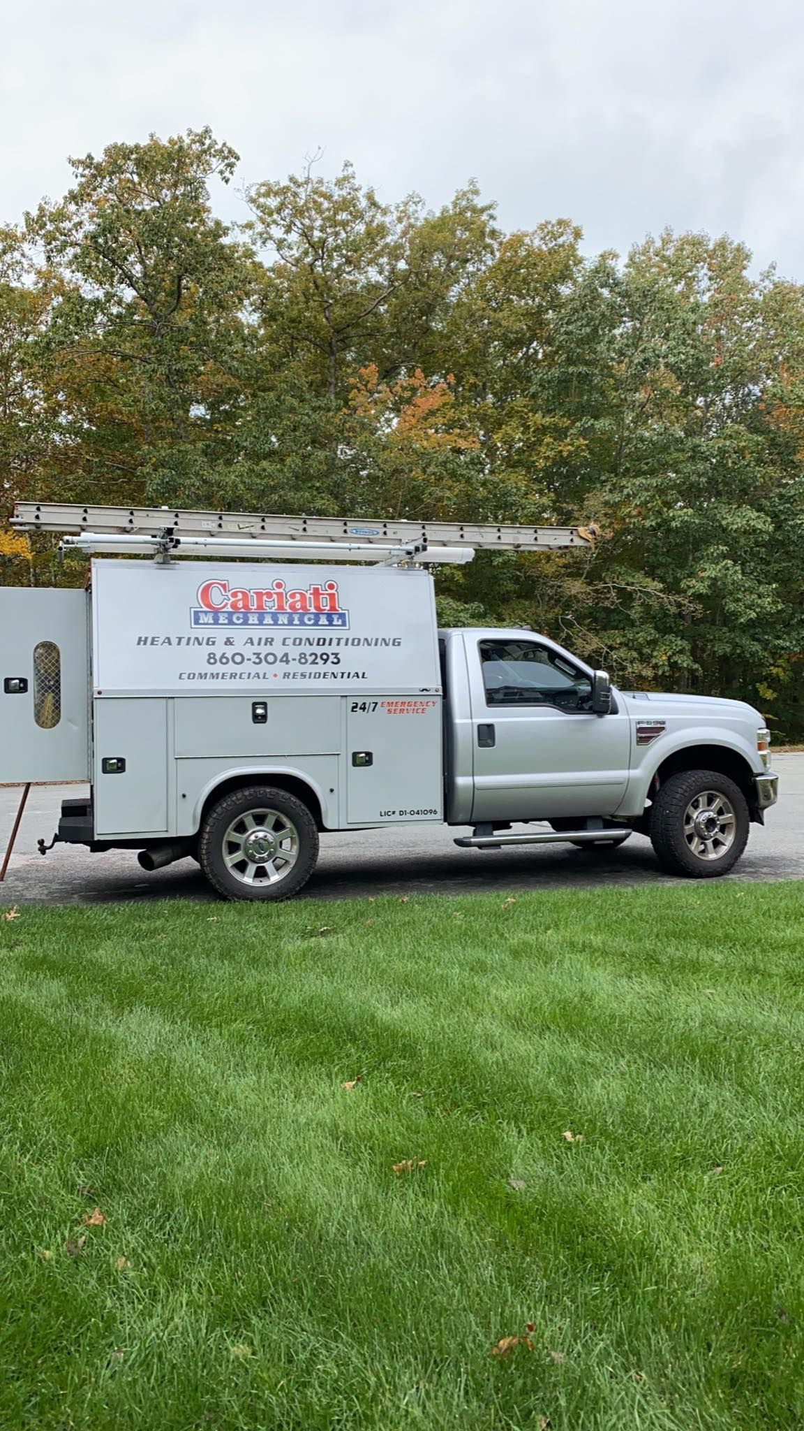 A white truck with a ladder on top of it is parked in a grassy field.