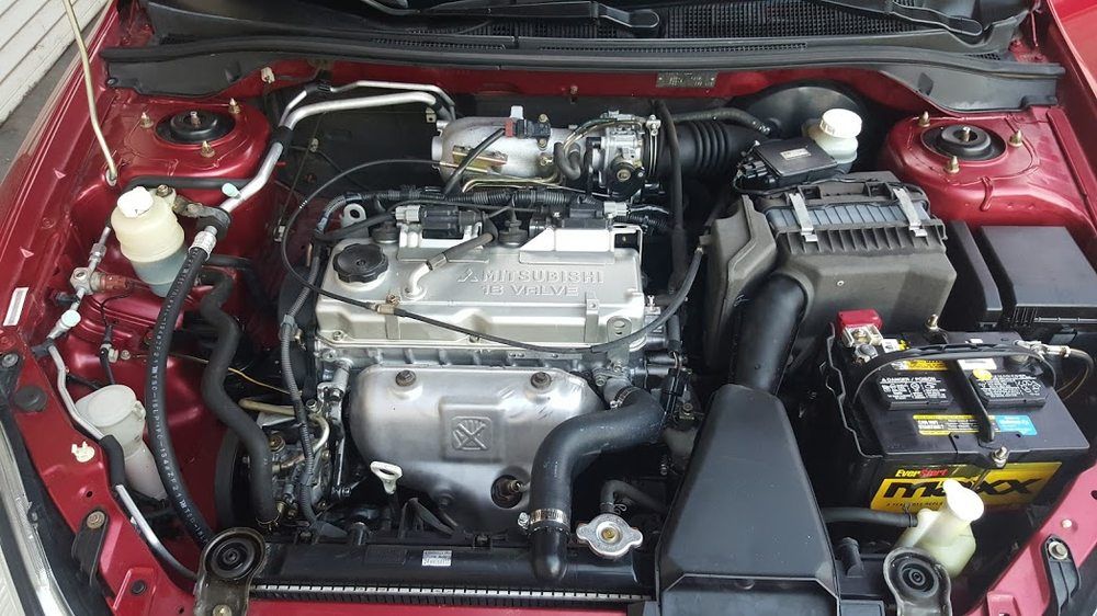 Car engine bay with silver components, black intake tubing, and battery in a red vehicle.