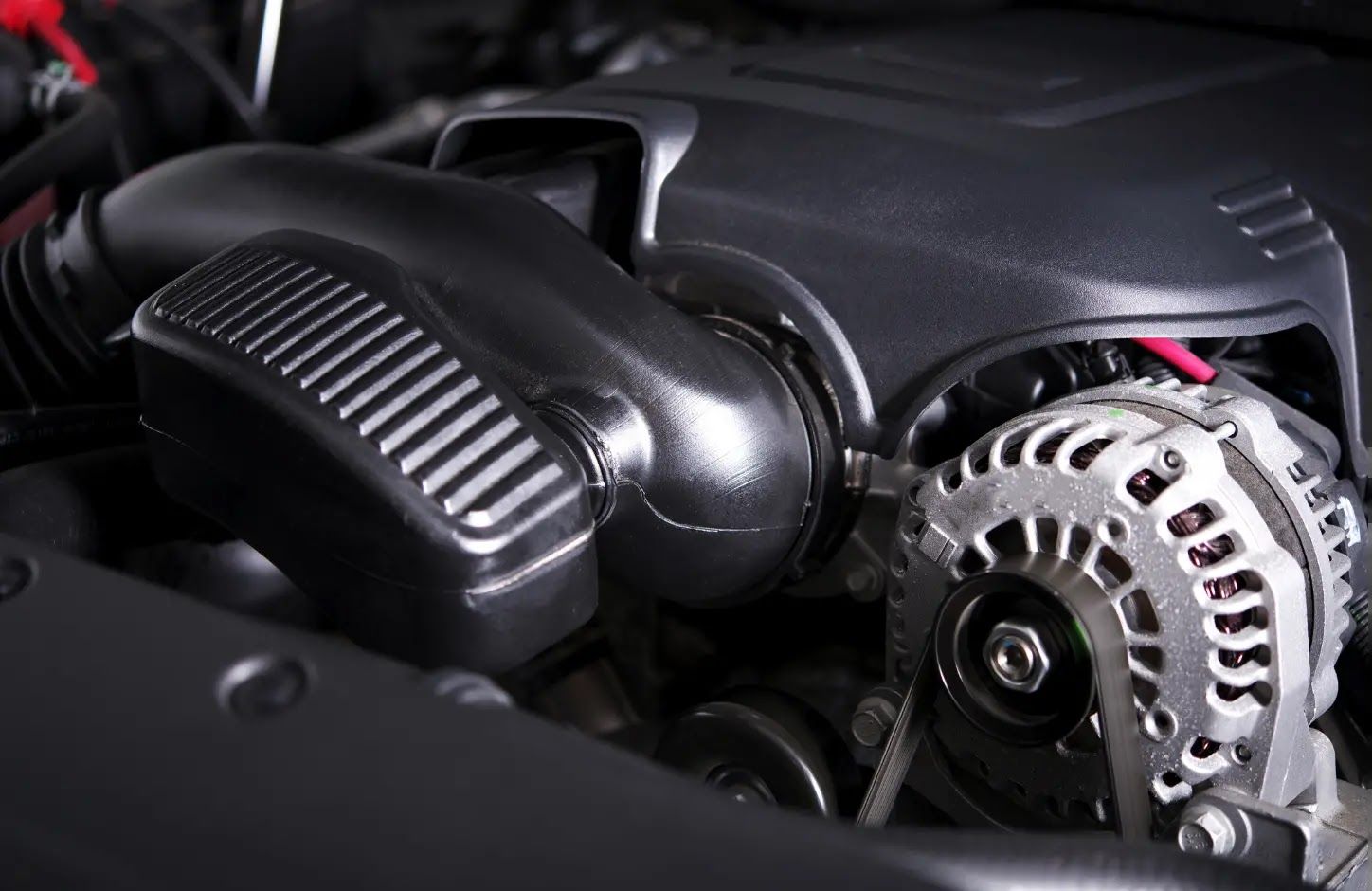 Close-up of a car engine, showing a black intake cover and silver alternator under the hood