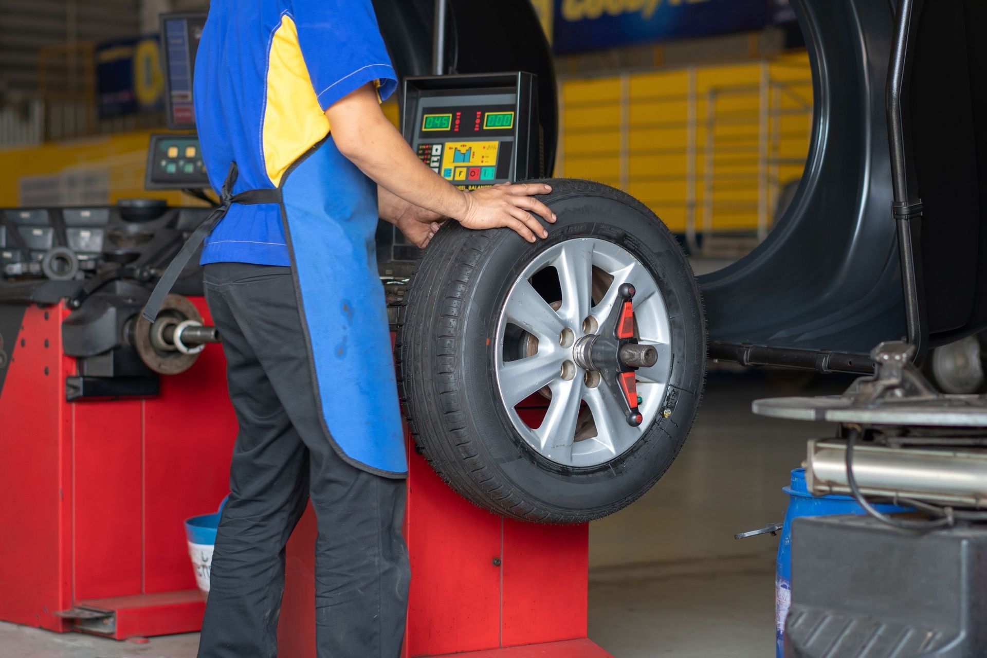 Mechanic balancing a car wheel at an auto shop, with a red tire machine in the background