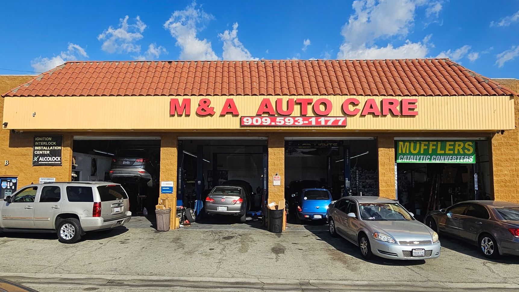 Auto repair shop with a car lifted on a jack and another blue car parked outside.