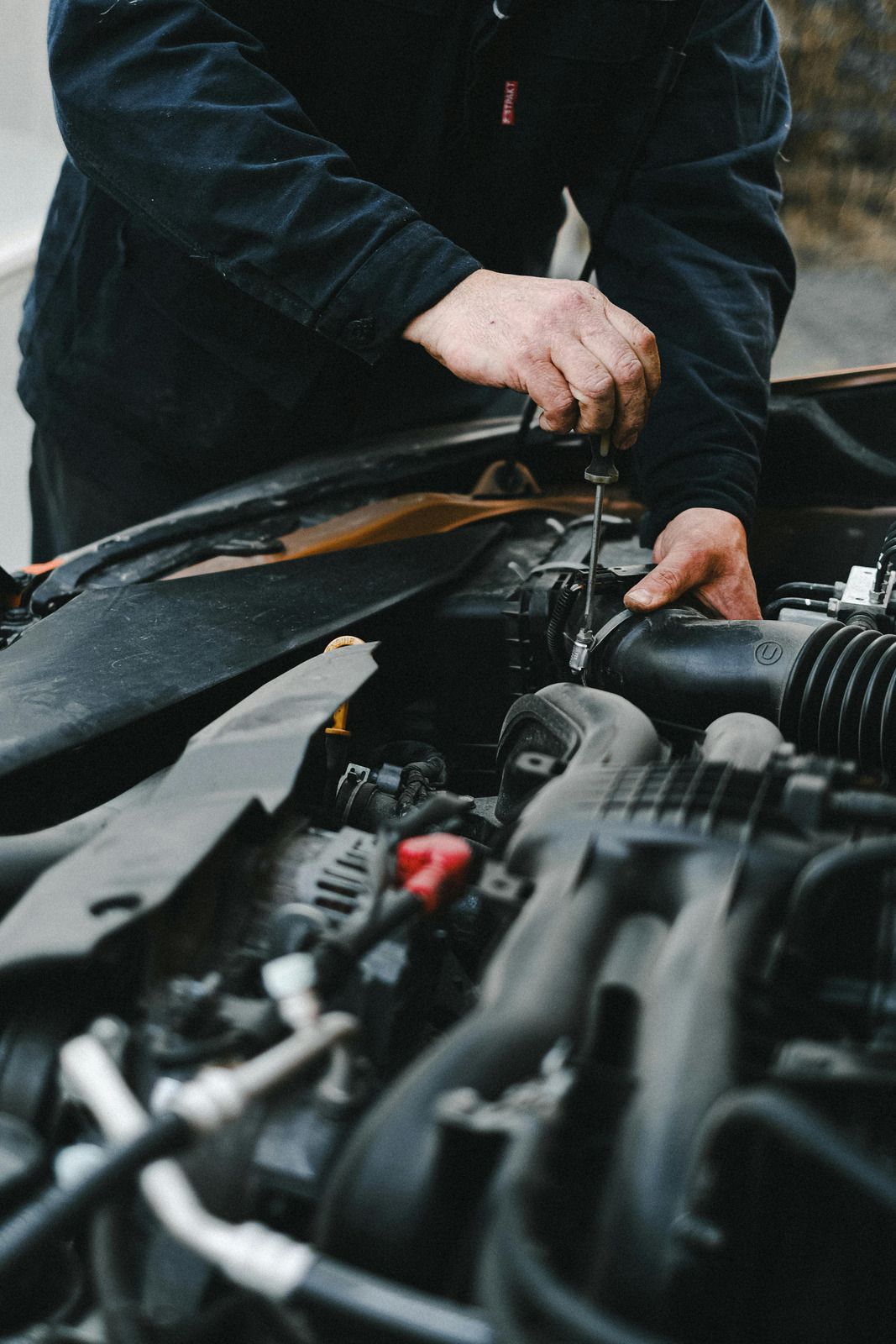 Person working under a car hood with a wrench in an outdoor setting
