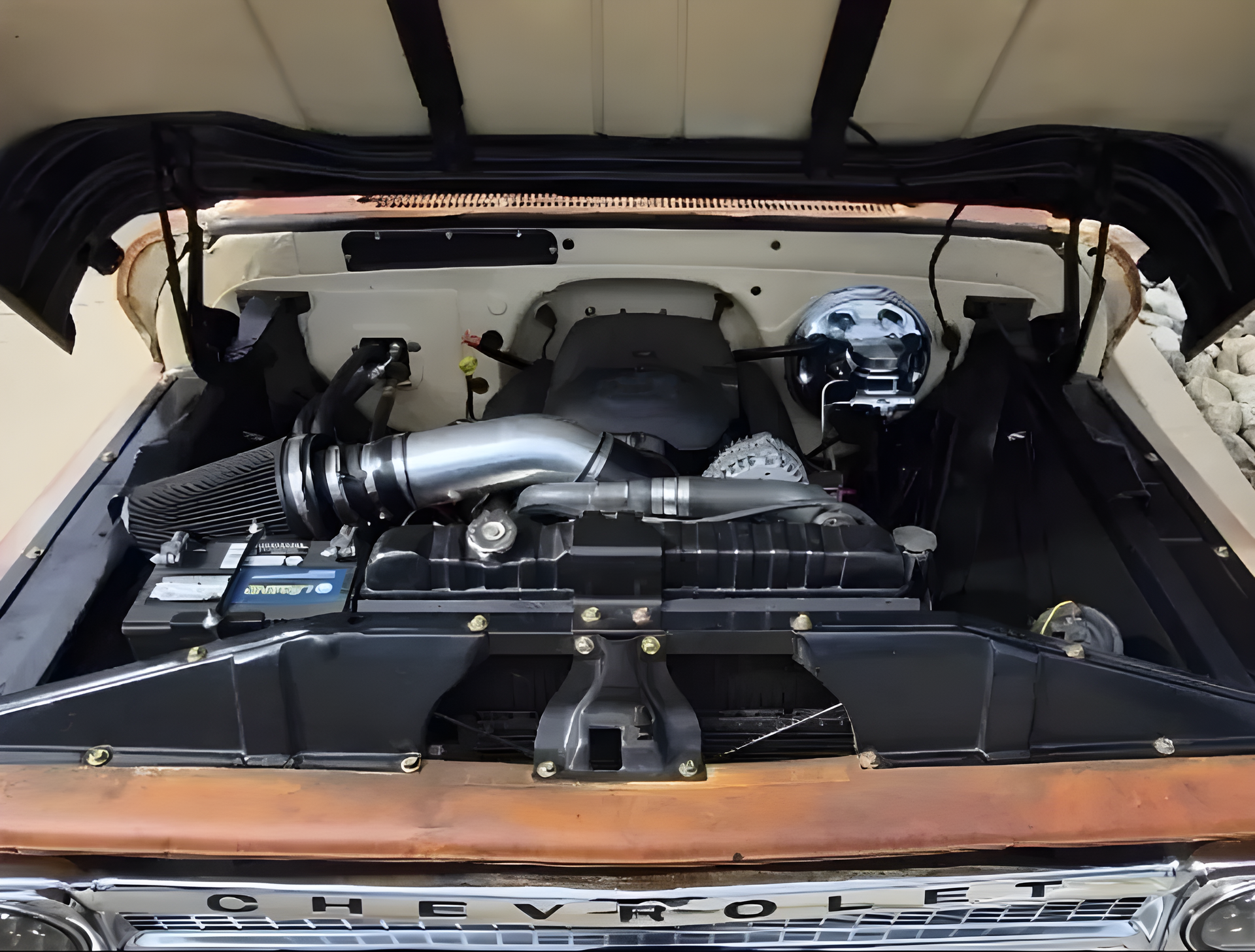 Classic car engine bay with a chrome air intake and black components under an open hood