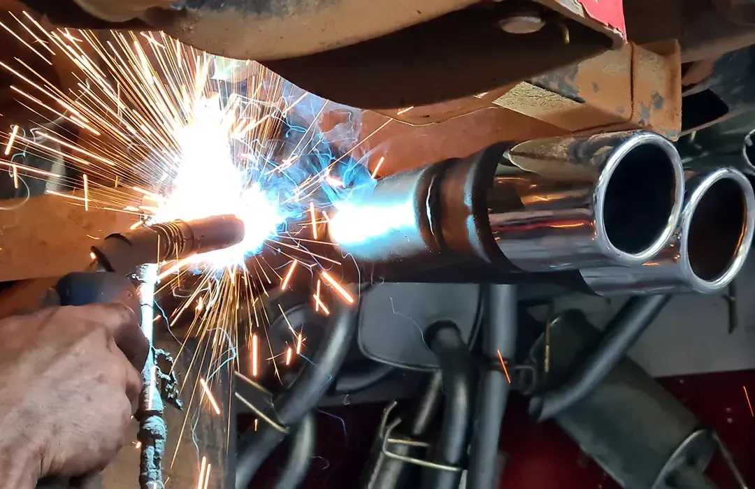 Mechanic in blue overalls using manifold gauges to service a car’s air conditioning system