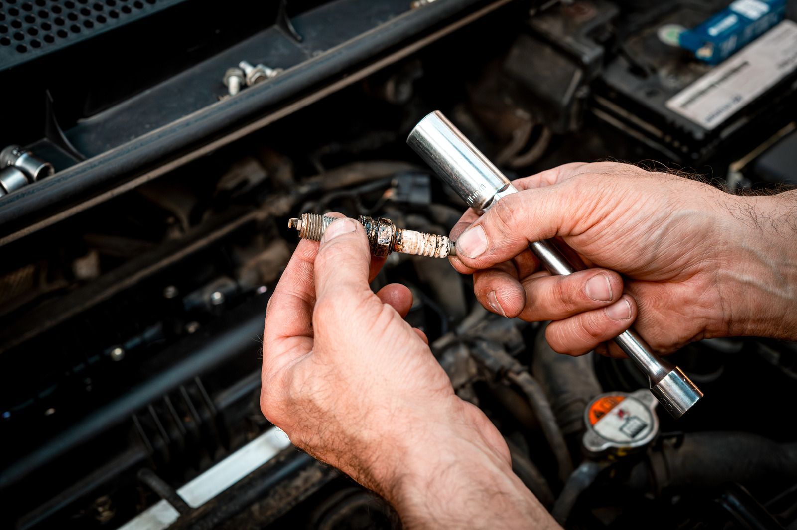 Hands using a socket wrench to loosen a car engine part under the hood