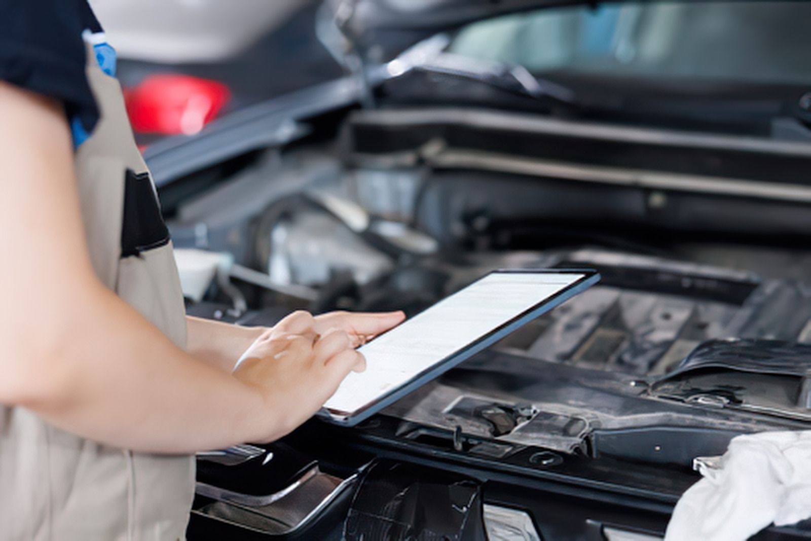 Mechanic inspecting an open car engine with a tablet