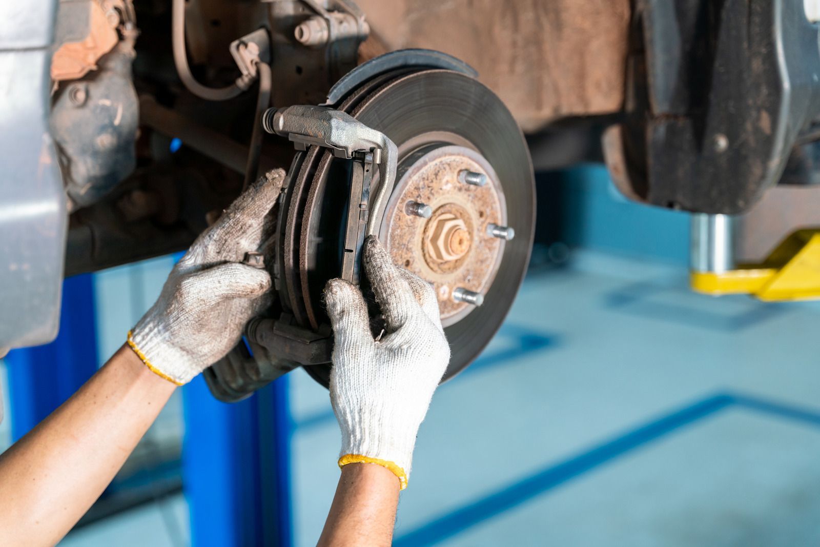 Mechanic’s gloved hands replacing a car brake pad on a lifted vehicle