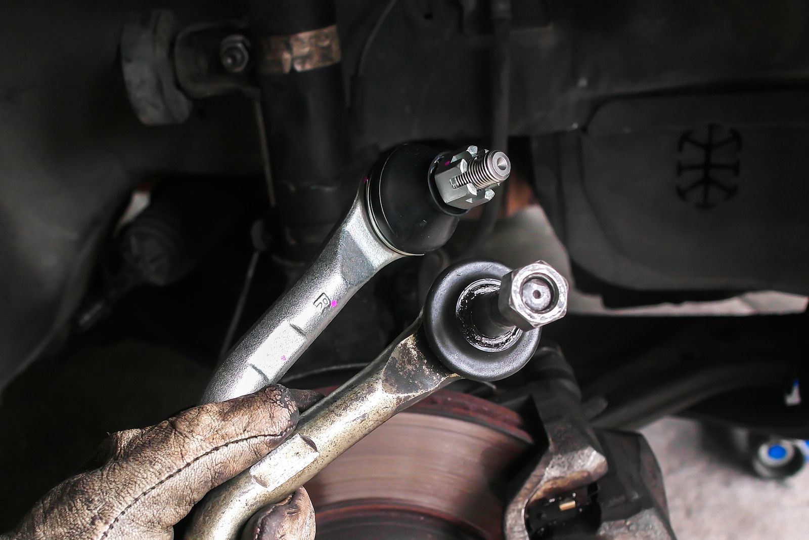 Worn wrench loosening a bolt on a brake rotor inside a car wheel well.