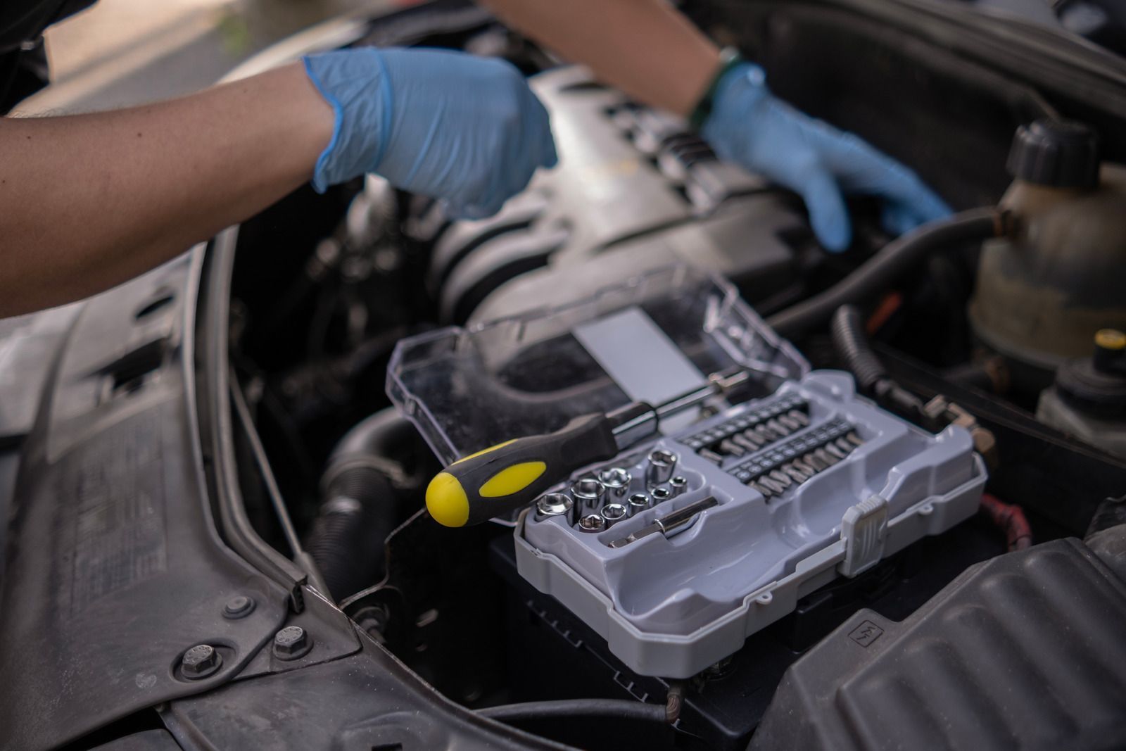 Mechanic’s gloved hands working on a car engine with a tool kit in the foreground