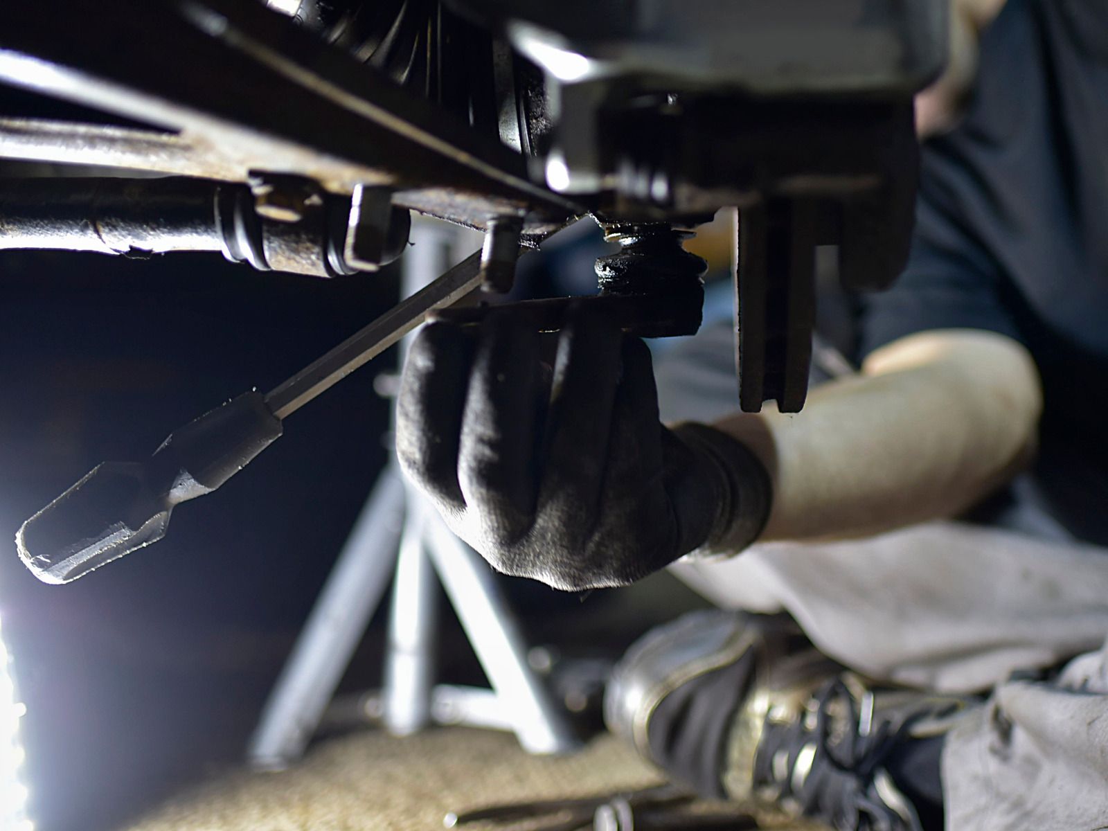 Gloved mechanic working under a vehicle, tightening a part with a wrench in a dim garage