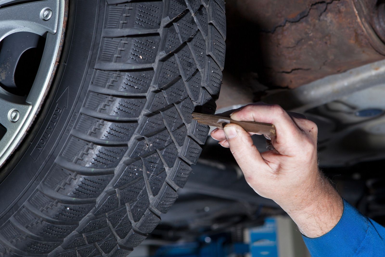 Hand checking tire tread with a gauge under a car