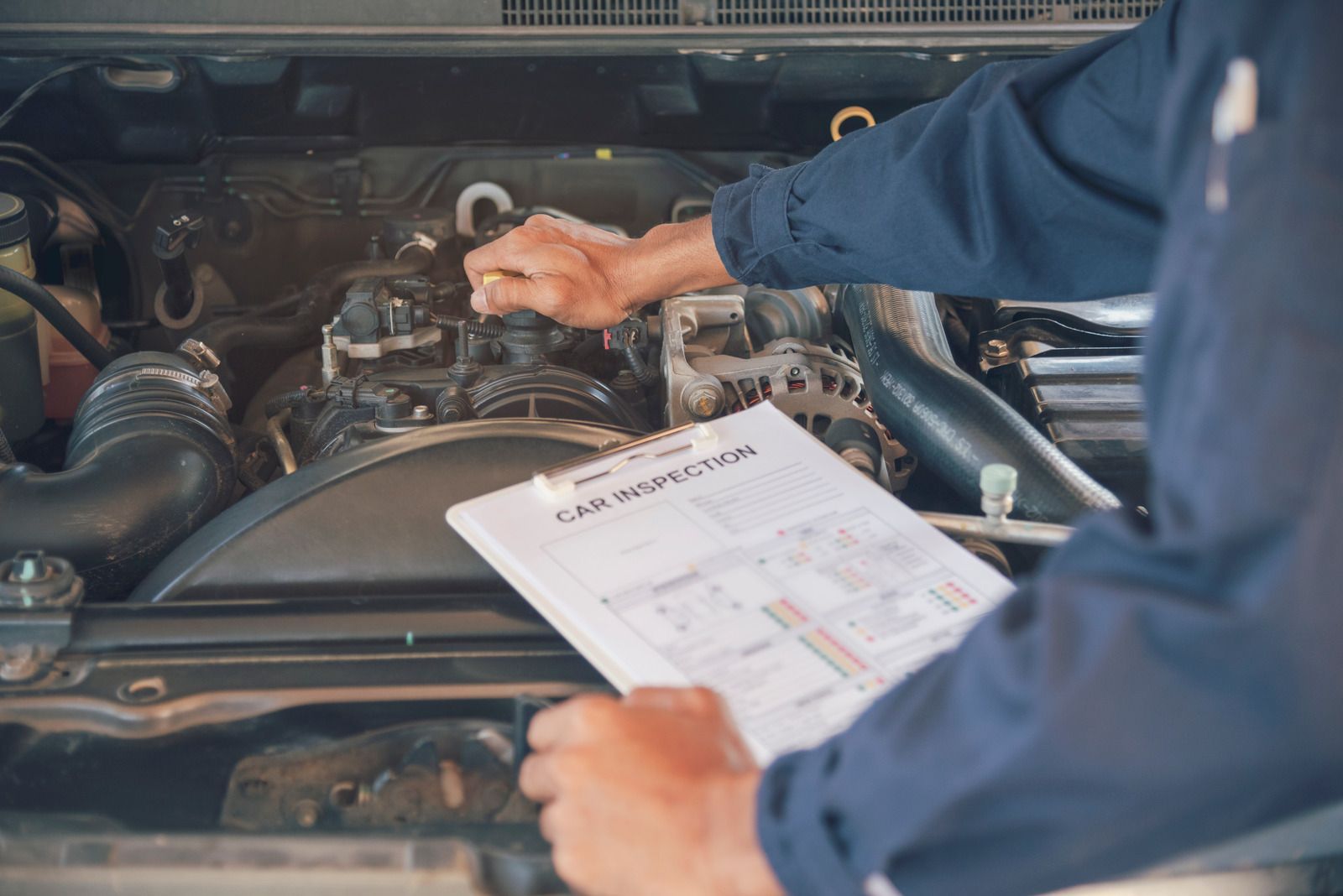 Mechanic inspecting a car engine while holding a checklist in a garage
