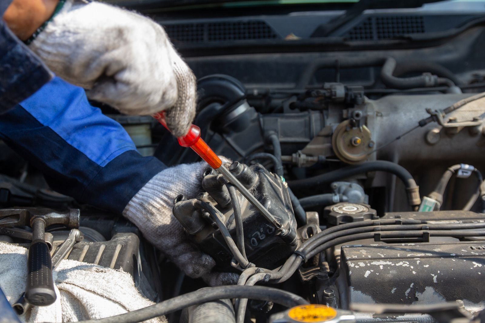 Mechanic using a screwdriver to repair car engine in an open hood compartment