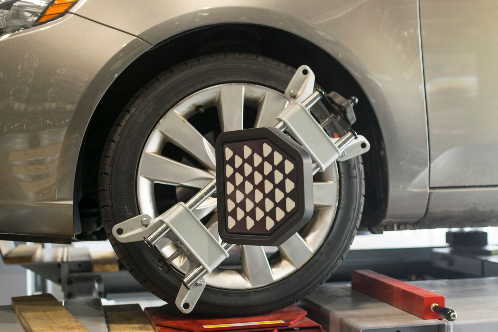Car wheel with alignment sensors mounted in an auto shop, next to a silver car.