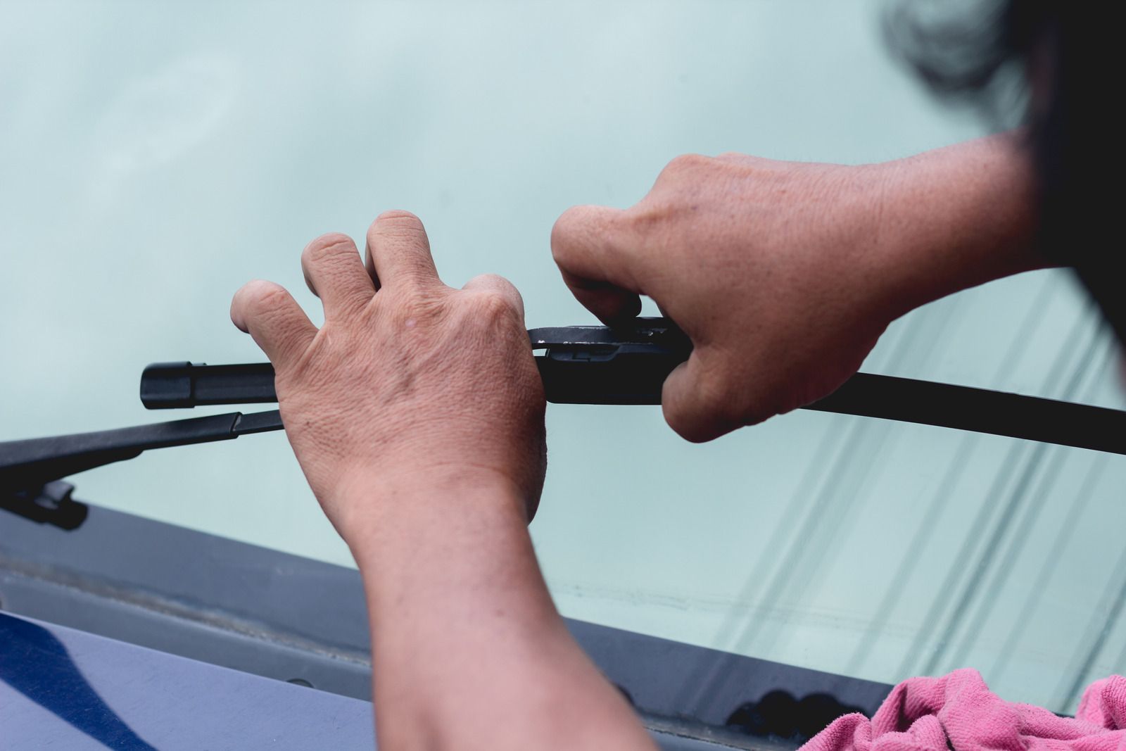 Hands adjusting a car windshield wiper on a windshield