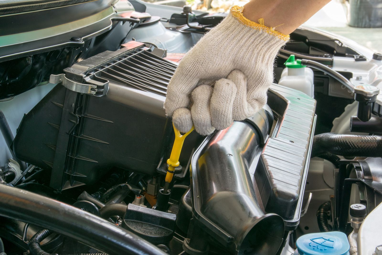 Gloved hand checking engine oil with a dipstick under an open car hood