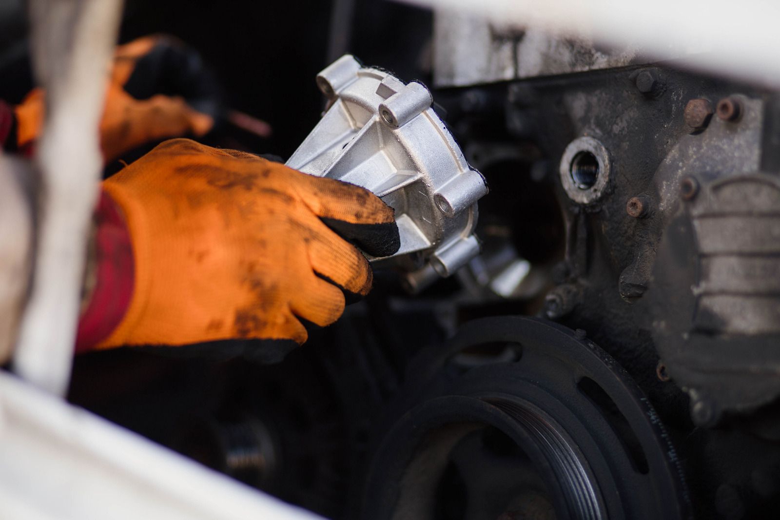 Orange-gloved hands handling a car engine part during repair