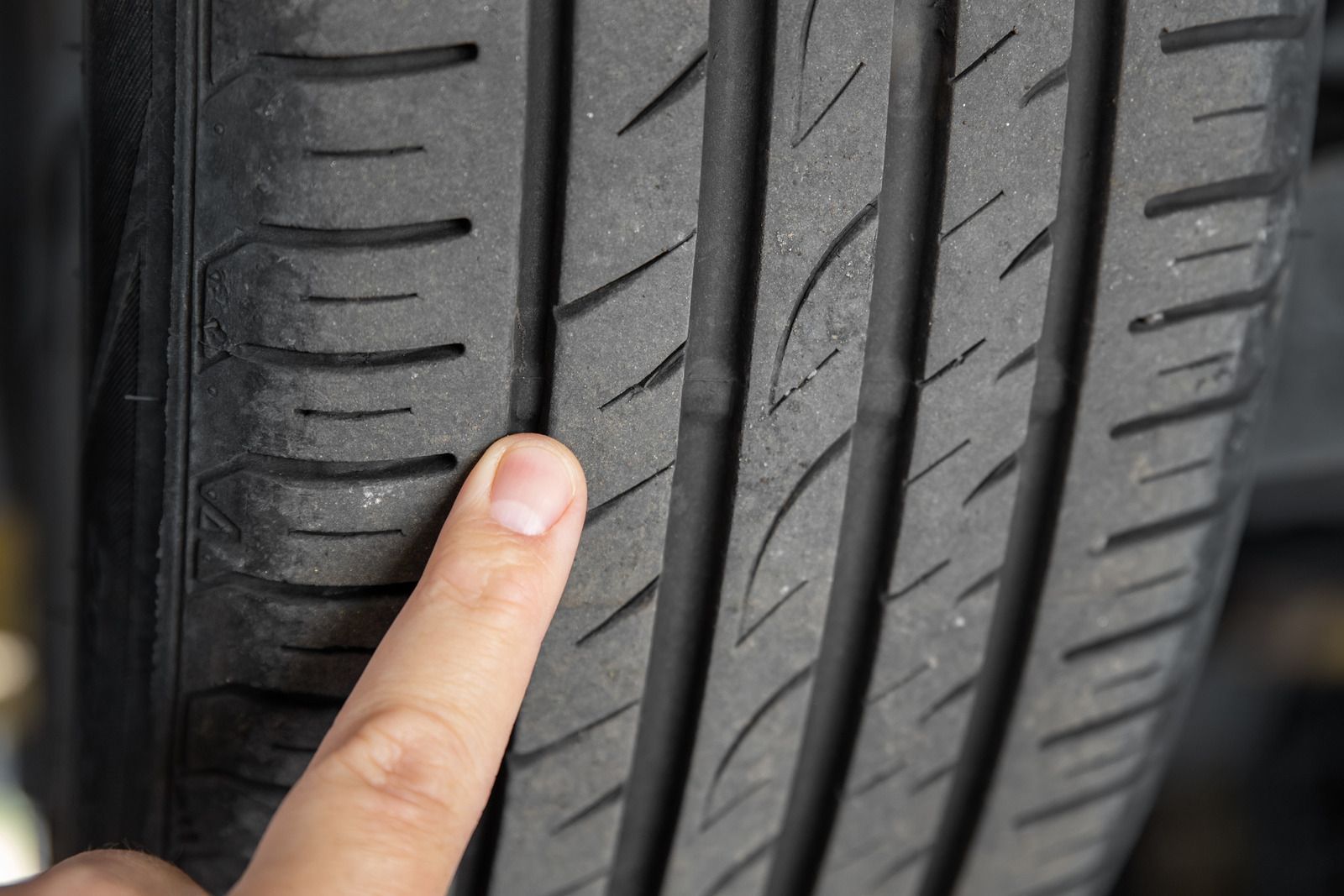 Finger pointing at a car tire tread wear indicator groove.