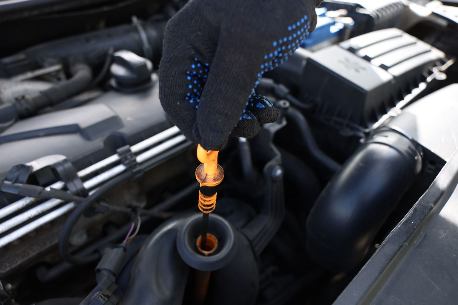 Gloved hand using an orange oil dipstick in a car engine bay