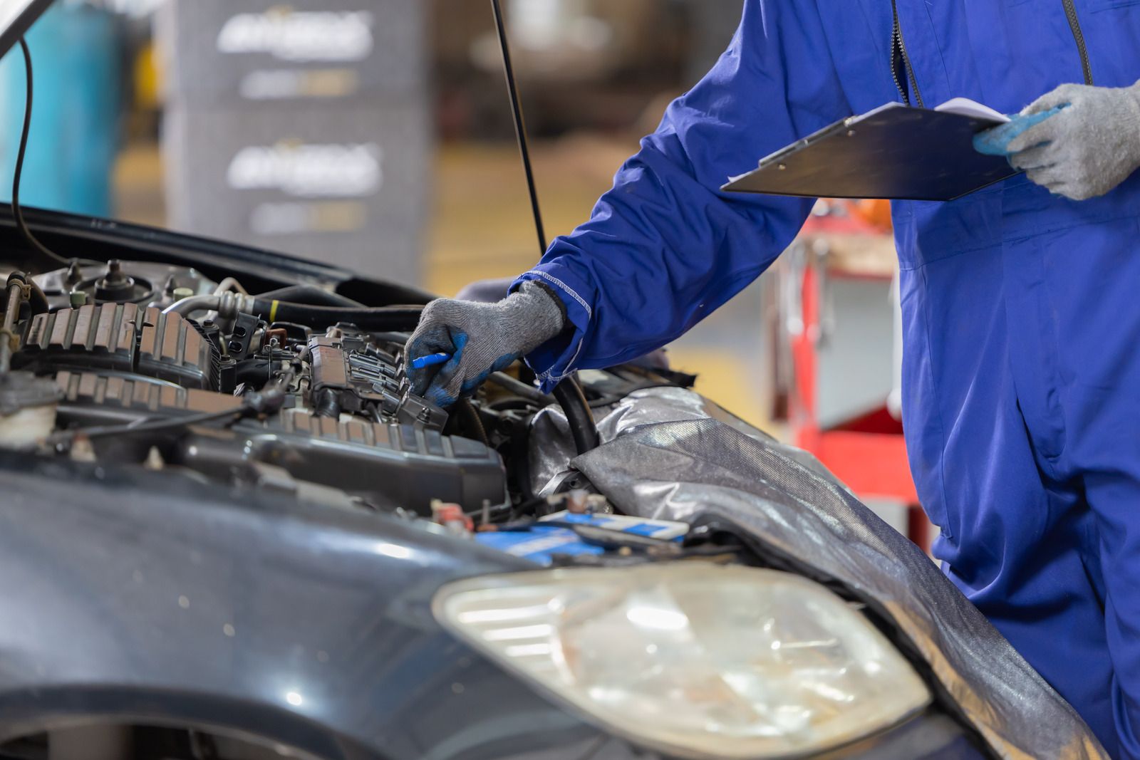 Mechanic in blue coveralls inspecting a car engine under the hood in a garage