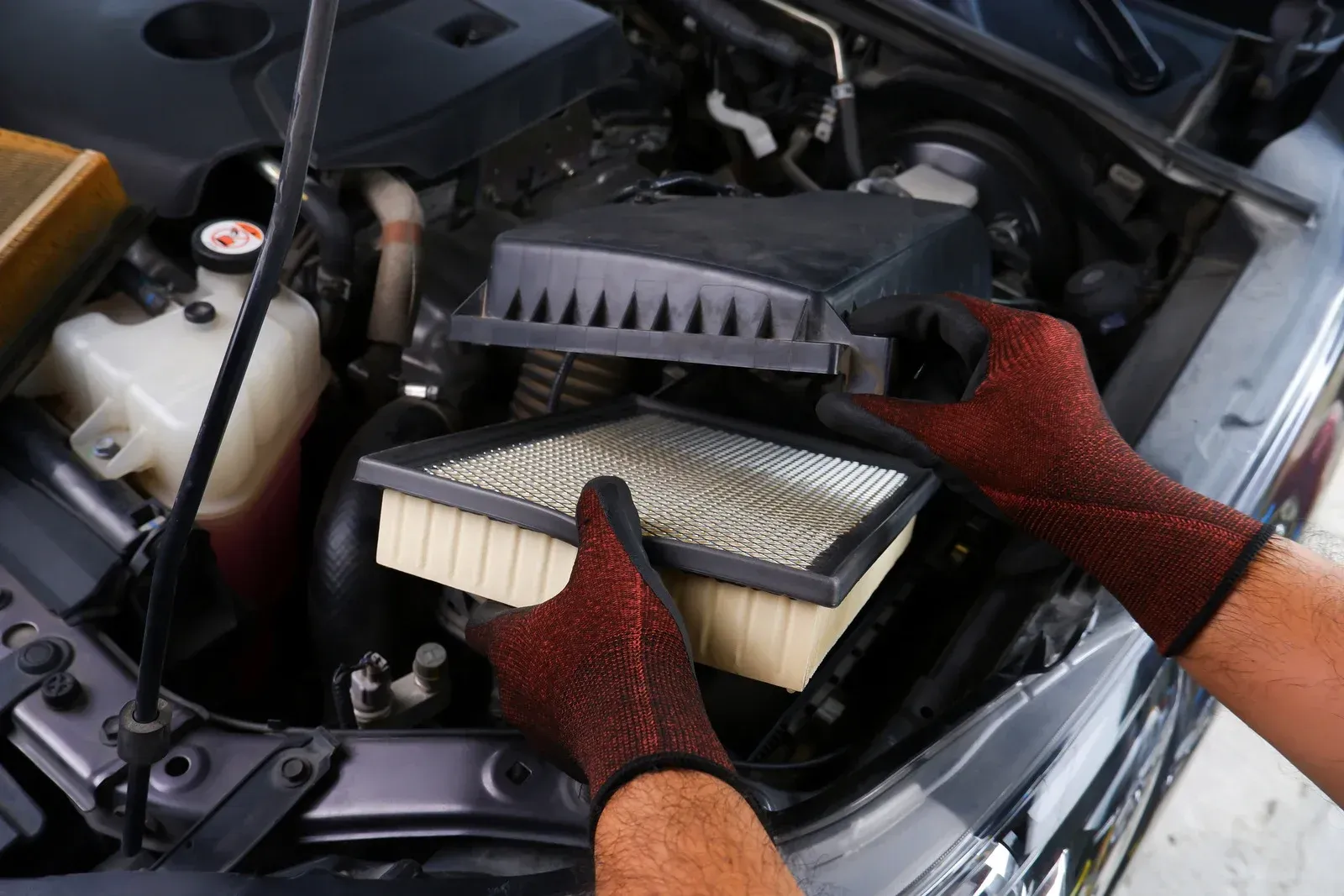 Hands replacing a bike air filter, with a black cover open above a white filter in an outdoor setting
