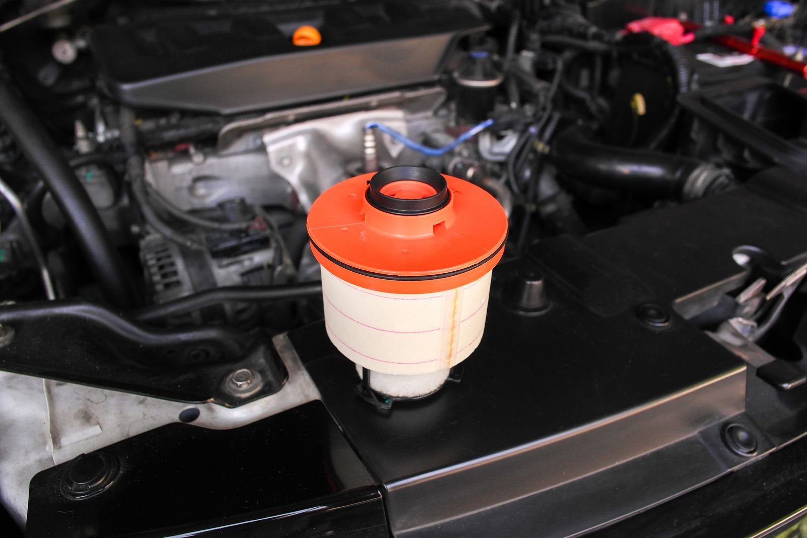 Car engine bay with a small white reservoir and orange cap in the foreground