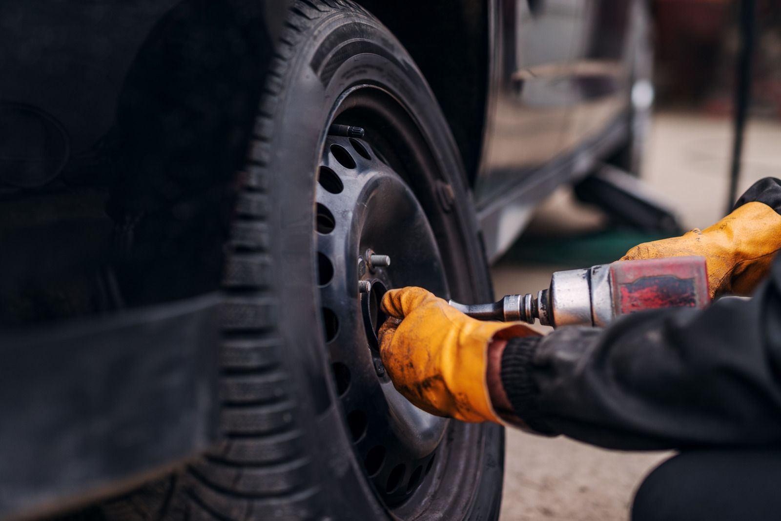 Mechanic in yellow gloves using a power tool to remove a car wheel lug nut