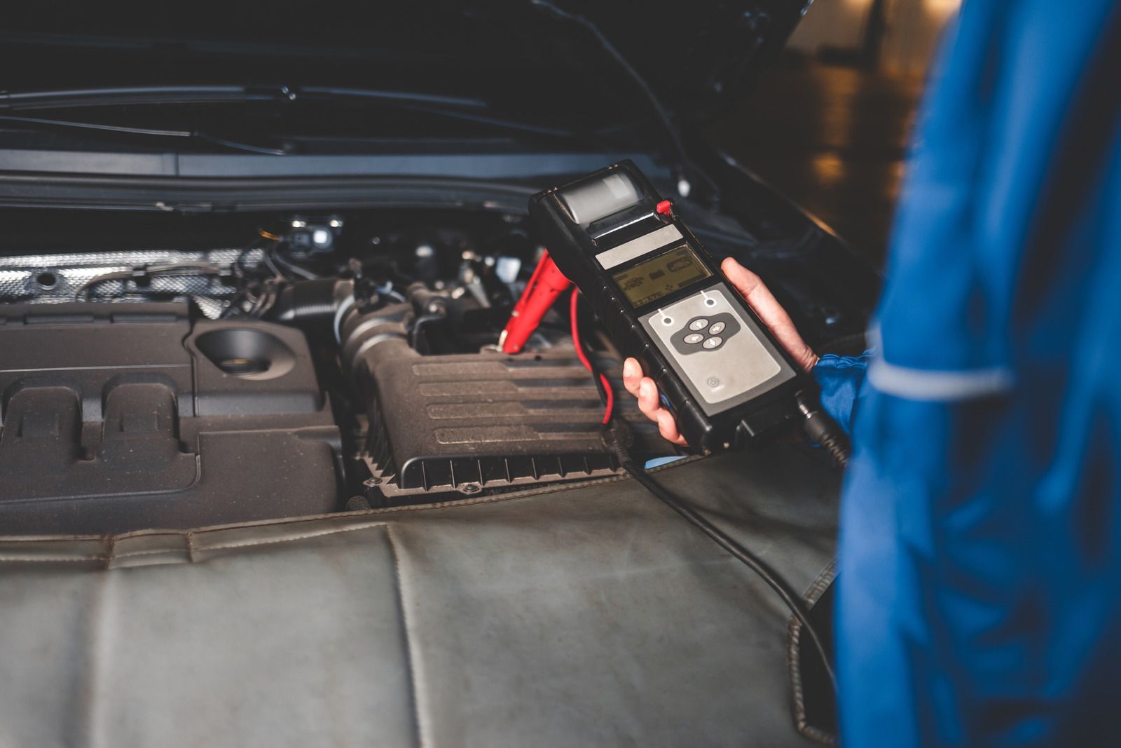 Car battery being tested with a handheld meter in an engine bay.