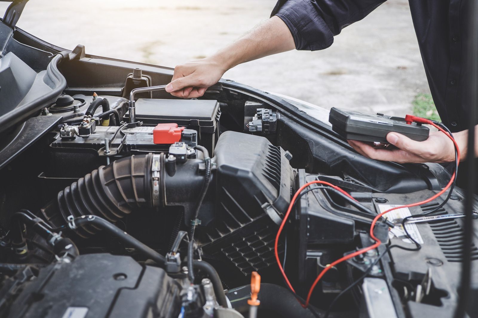 Mechanic jump-starting a car engine with red and black jumper cables under the hood