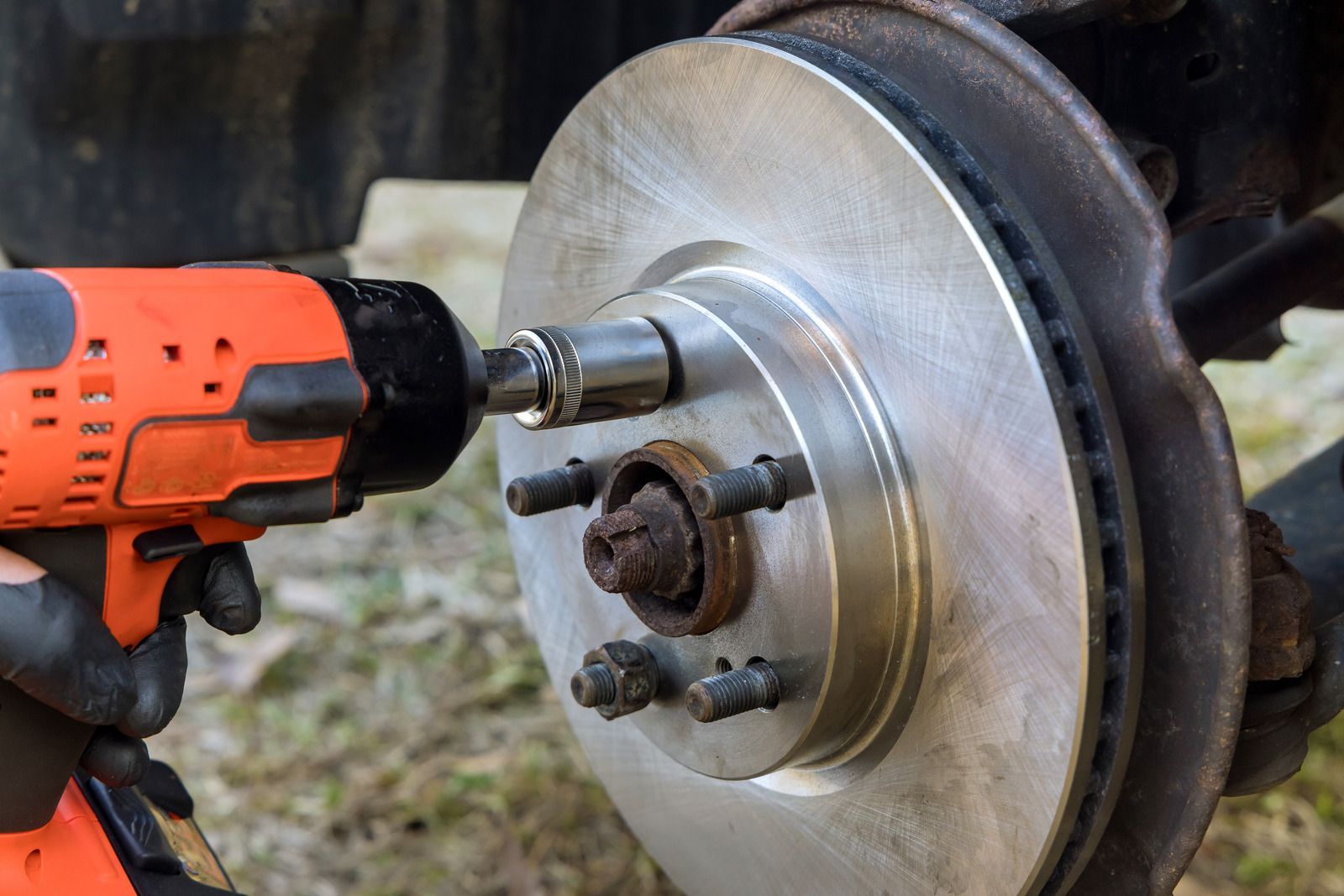 Orange impact wrench loosening lug nuts on a car wheel hub with brake rotor