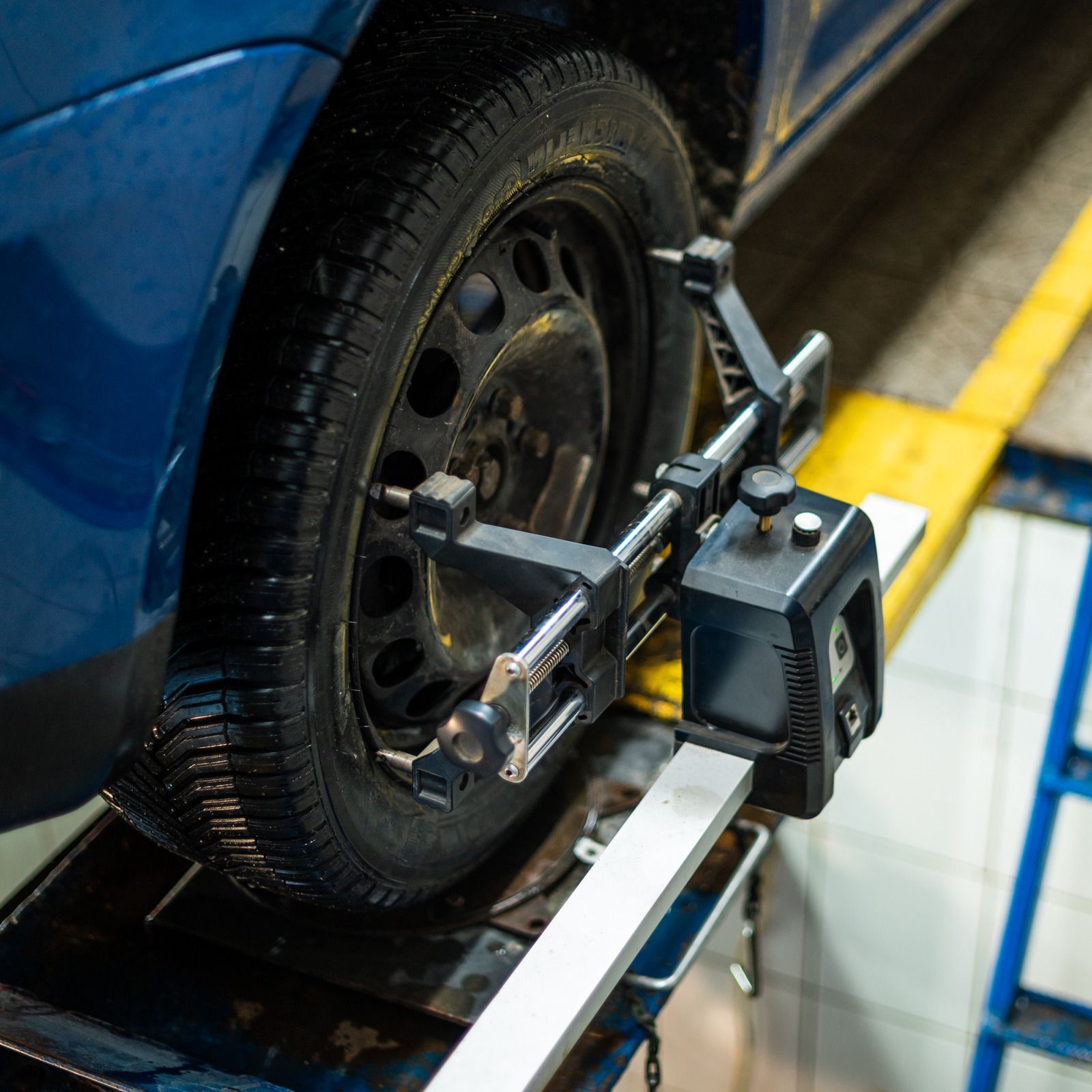Car wheel on alignment machine in a blue auto shop, with measuring arms attached