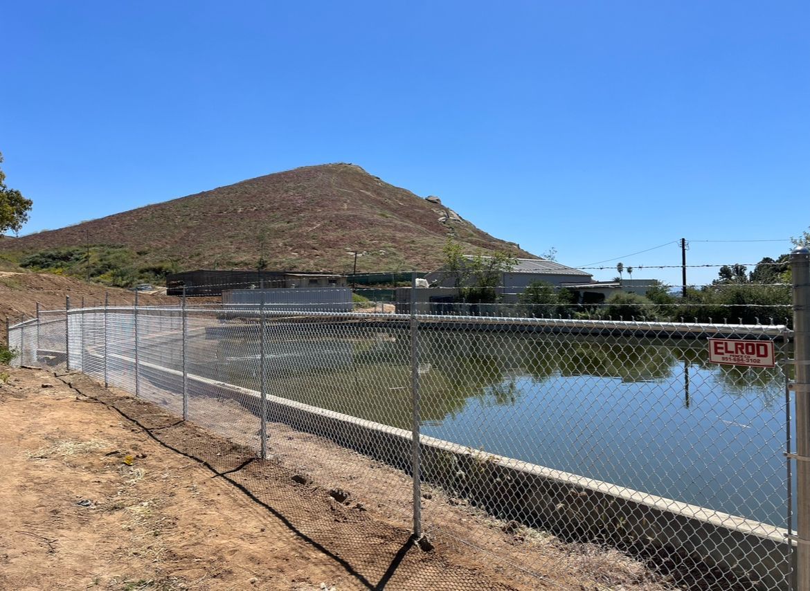 A Chain Link Fence Surrounds a Pond With a Mountain in the Background — Riverside, CA — Elrod Fence Co