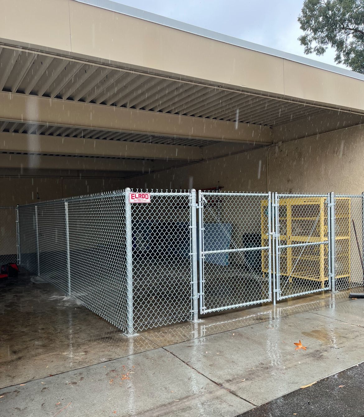 Chain-link fence enclosure under a building overhang in the rain.