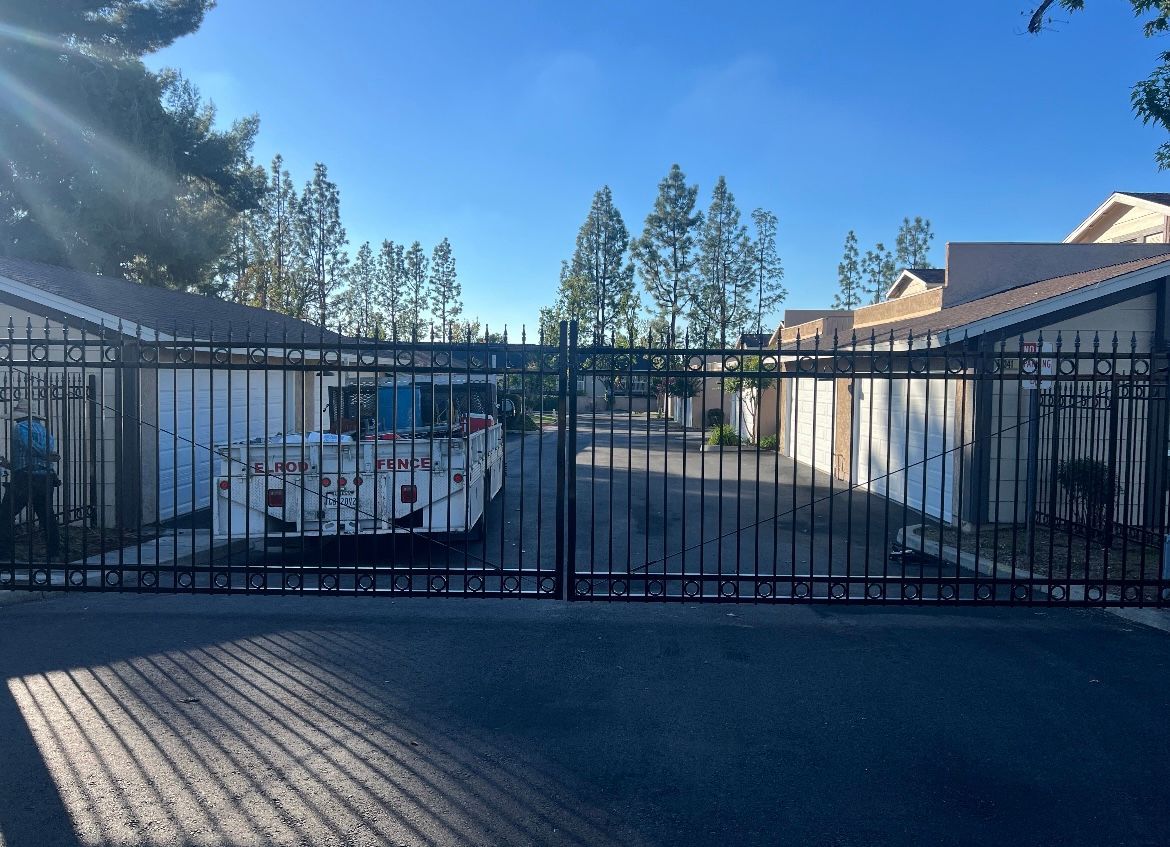 A car is parked in a driveway behind a wrought iron gate.