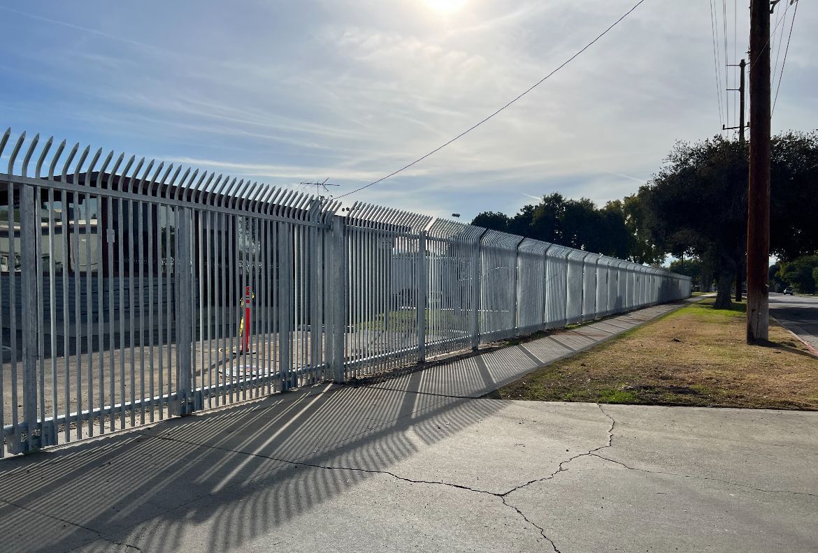 A fence is along the side of a road next to a sidewalk.