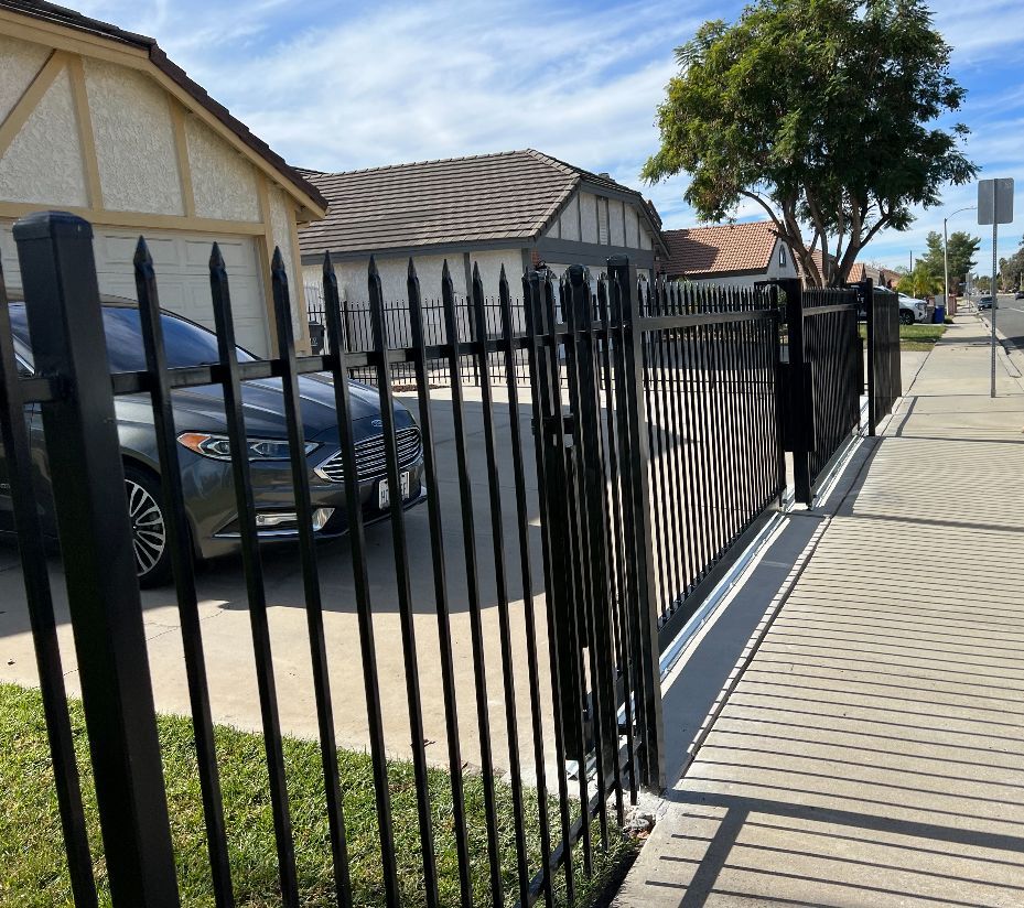 A car is parked behind a black fence in front of a house