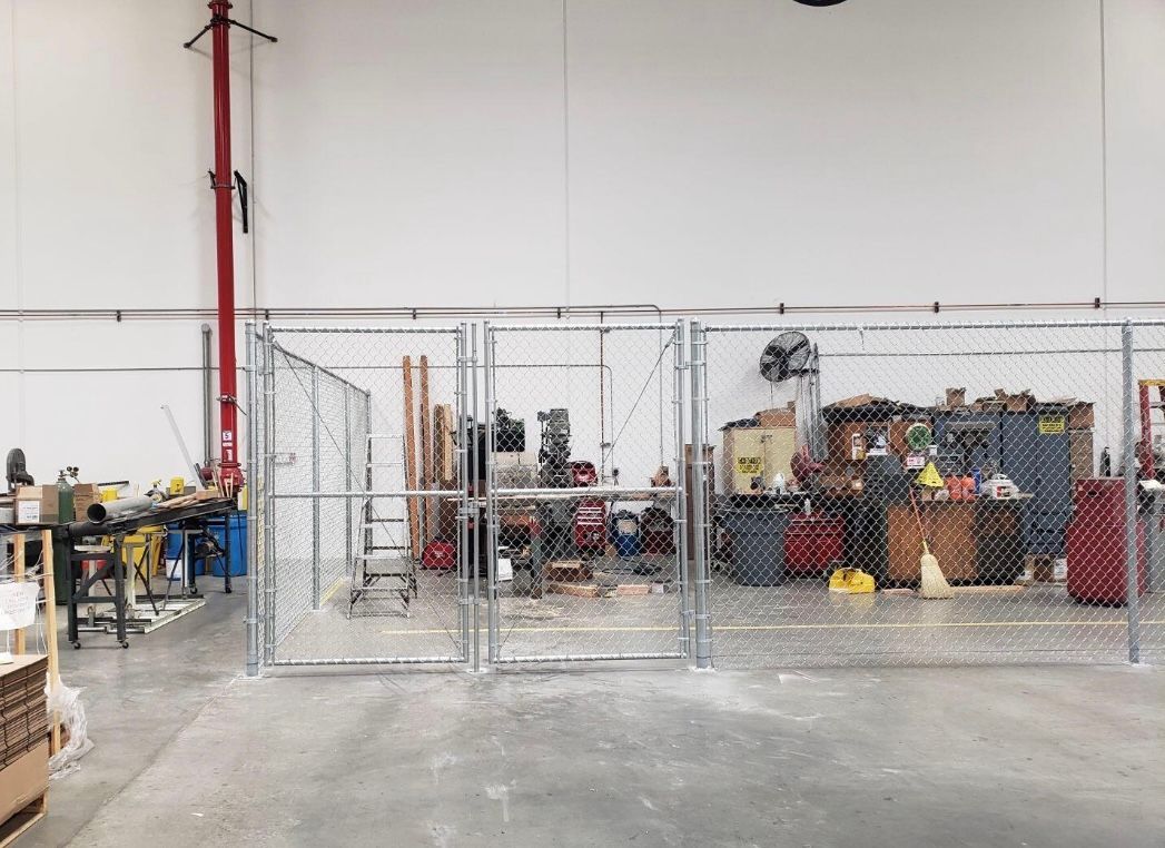 A fenced-in area inside a large warehouse. The area contains equipment and clutter.