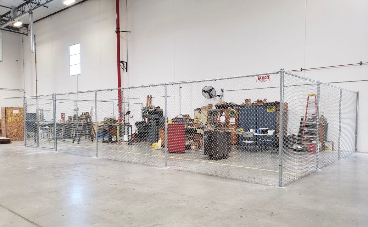 Chain-link fence encloses workshop tools and equipment in a warehouse.