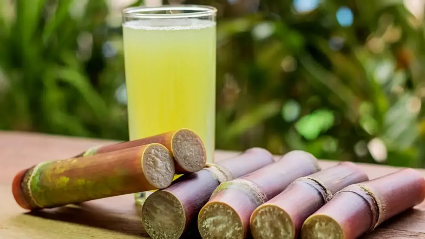 There is a glass of sugarcane juice next to a pile of sugarcane sticks.