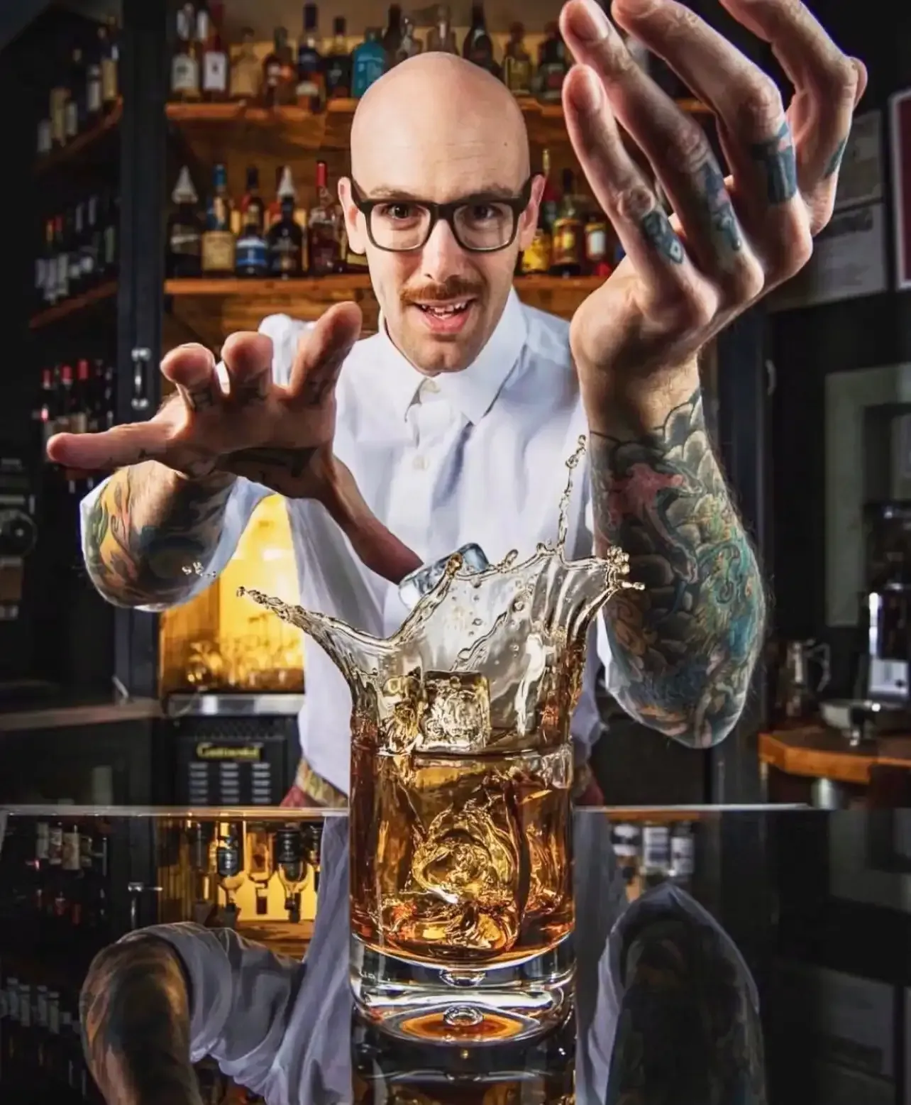 A man with glasses is splashing a drink into a glass