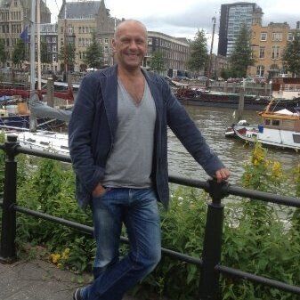 Een man die naast een reling staat met boten op de achtergrond