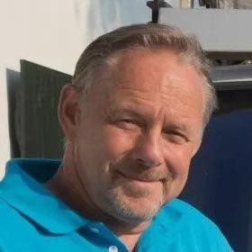 Een man met een baard draagt een blauw shirt en glimlacht.