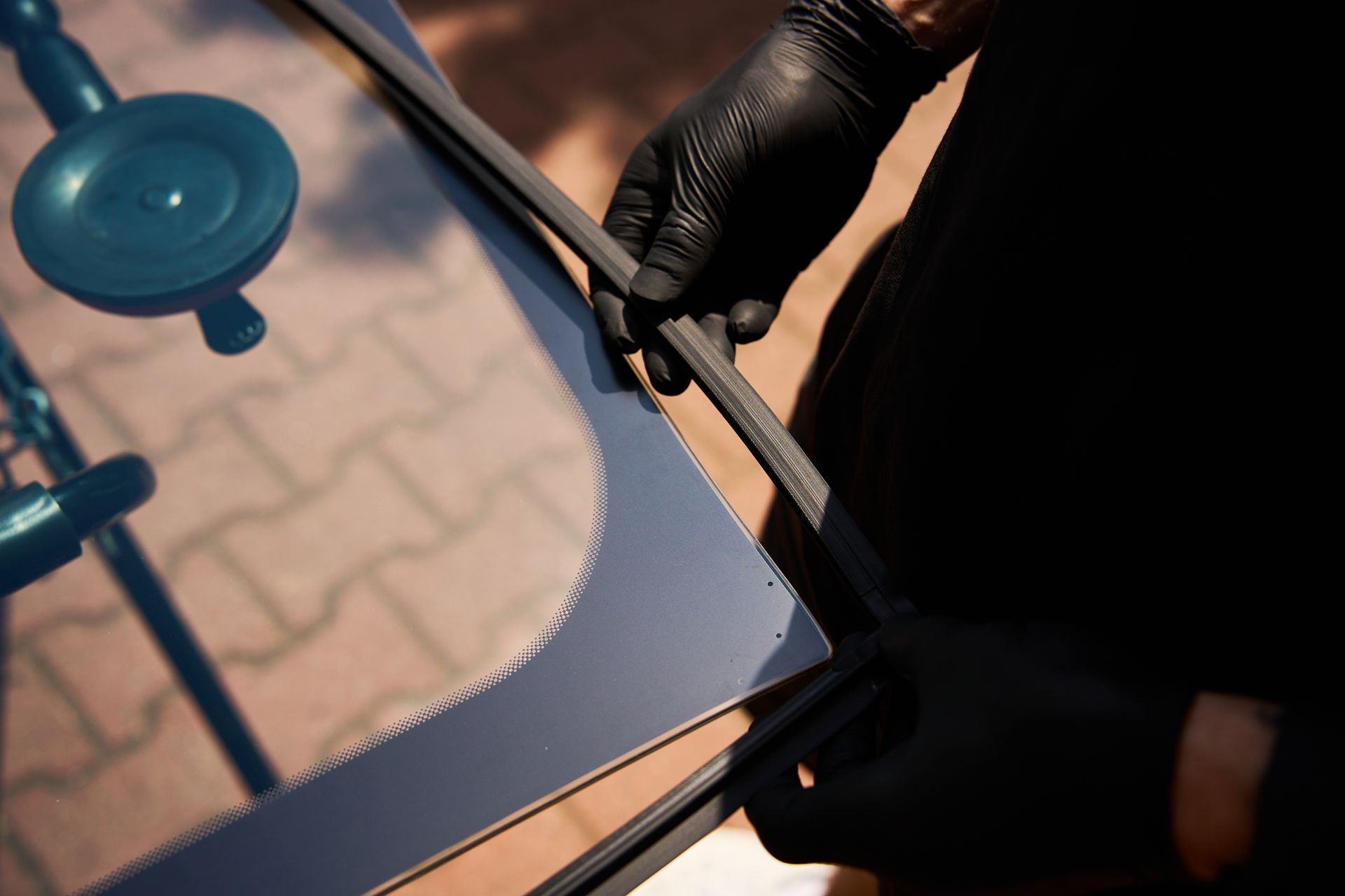 Gloved hands installing a rubber trim or seal along the edge of an automotive windshield.