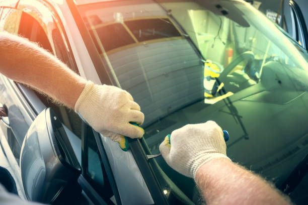 Person in gloves using tools to remove car windshield seal.