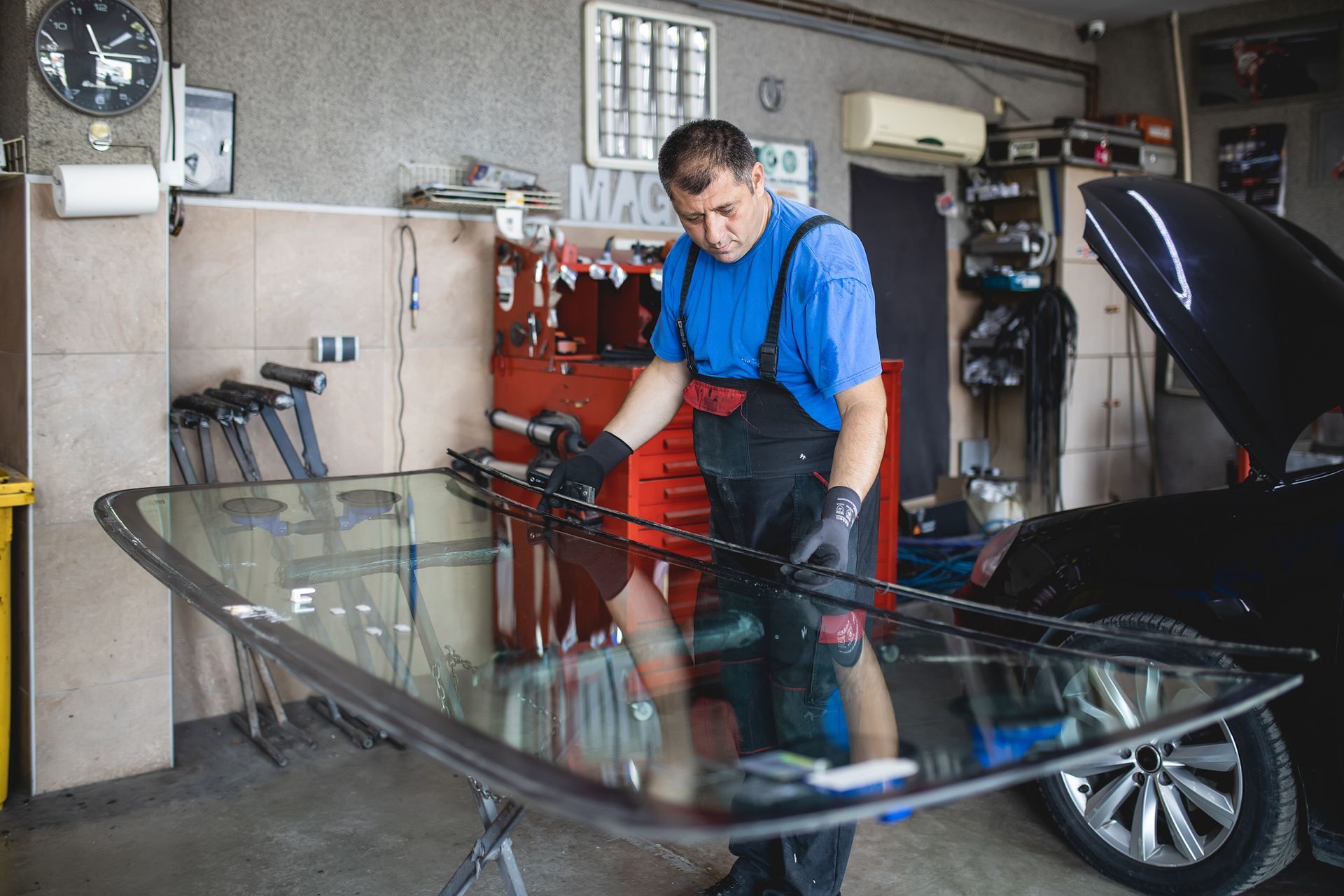 Mechanic in blue overalls installing windshield in a garage.