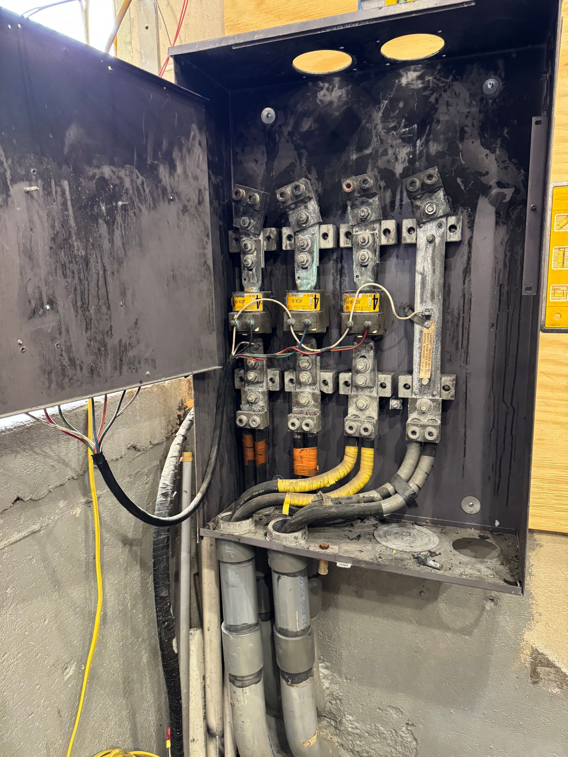 Electrician on ladder, inspecting equipment in an electrical control room. Panels, meters, and a computer on a toolbox are visible.