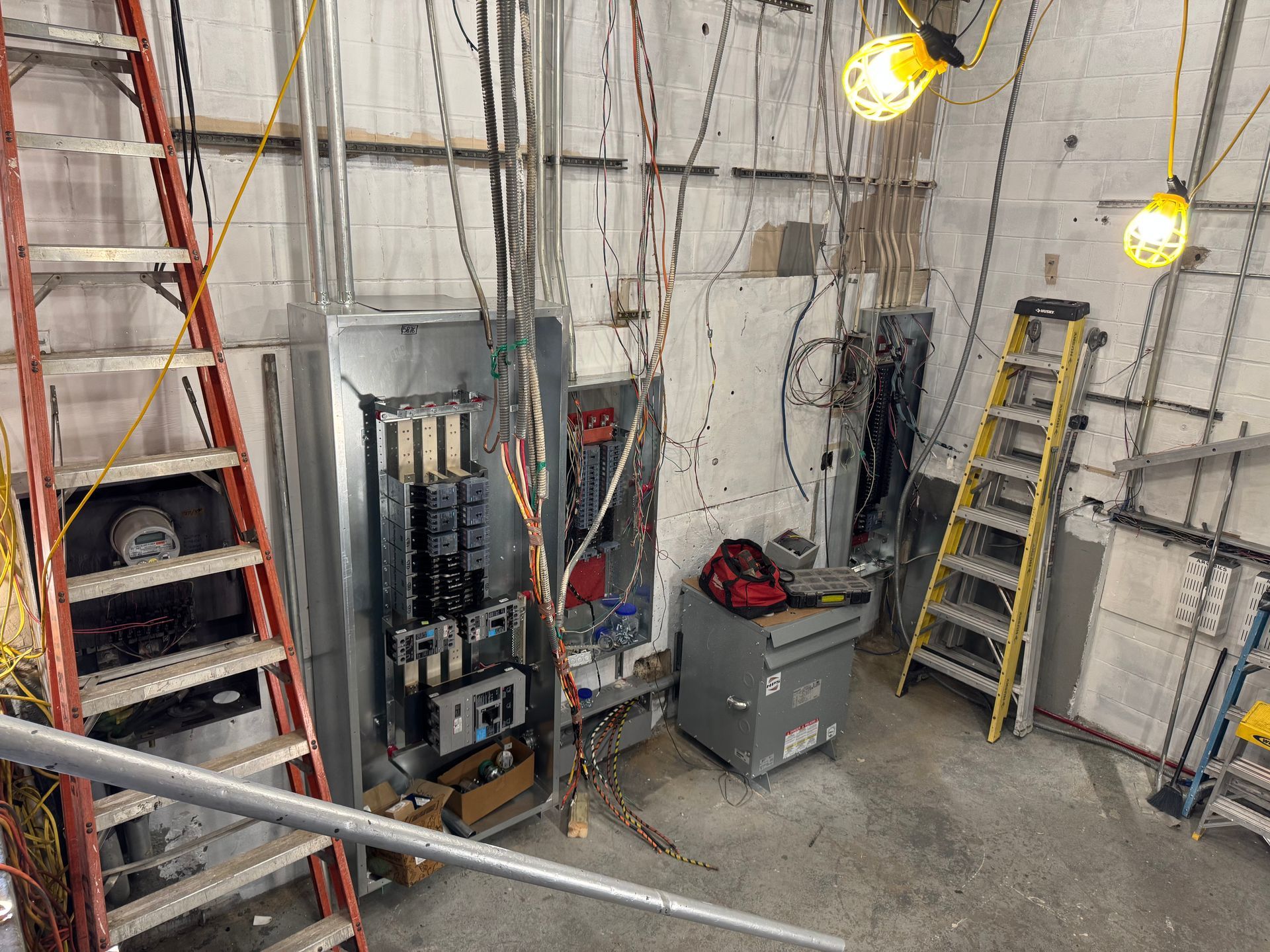 Man in orange work suit, face shield, and gloves working on electrical box outdoors.