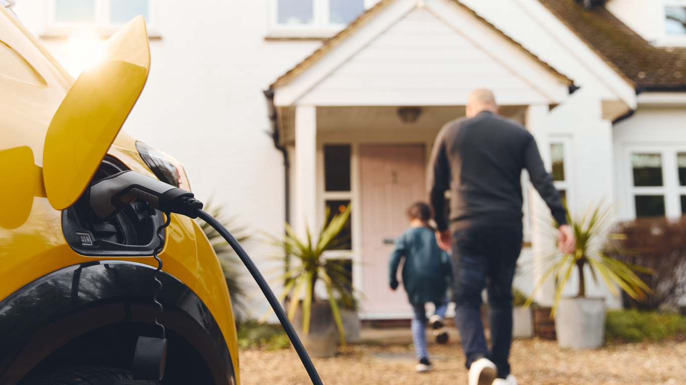 Yellow electric car charging at a home. A man and child walk toward the house.